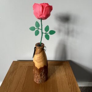 A vibrant pink 3D-printed rose with green leaves, elegantly displayed in a handcrafted wooden vase, illustrating the blend of traditional craftsmanship and innovative 3D printing